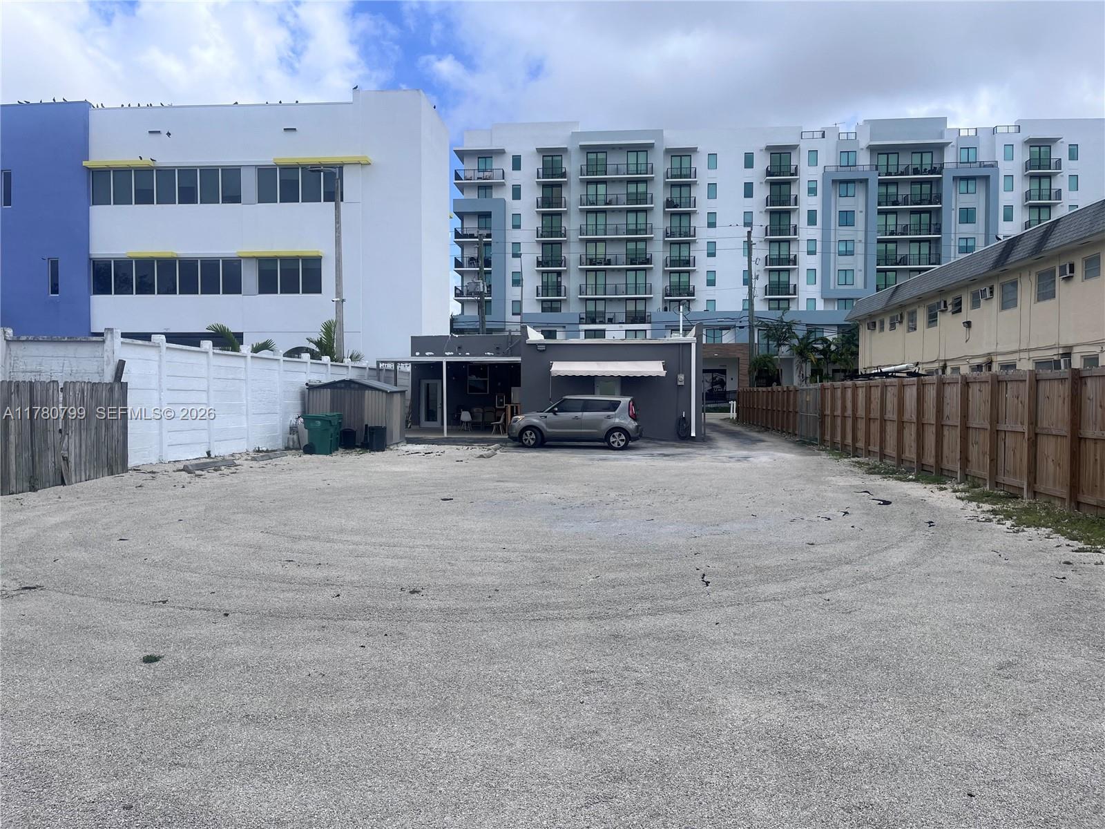 A gravel parking lot sits in front of a small gray building and larger structures — 2228 SW 67th Ave, Miami FL 33155, MIAMI, FL