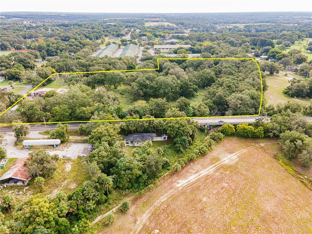 An aerial view shows a large, wooded lot outlined in yellow near a road and bridge — 610 S HIGHLAND STREET, MOUNT DORA, FL