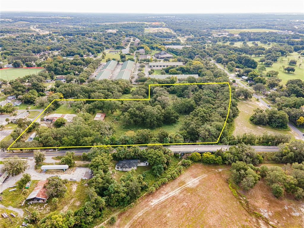 An aerial view shows a large, wooded plot of land outlined in yellow near a road — 610 S HIGHLAND STREET, MOUNT DORA, FL