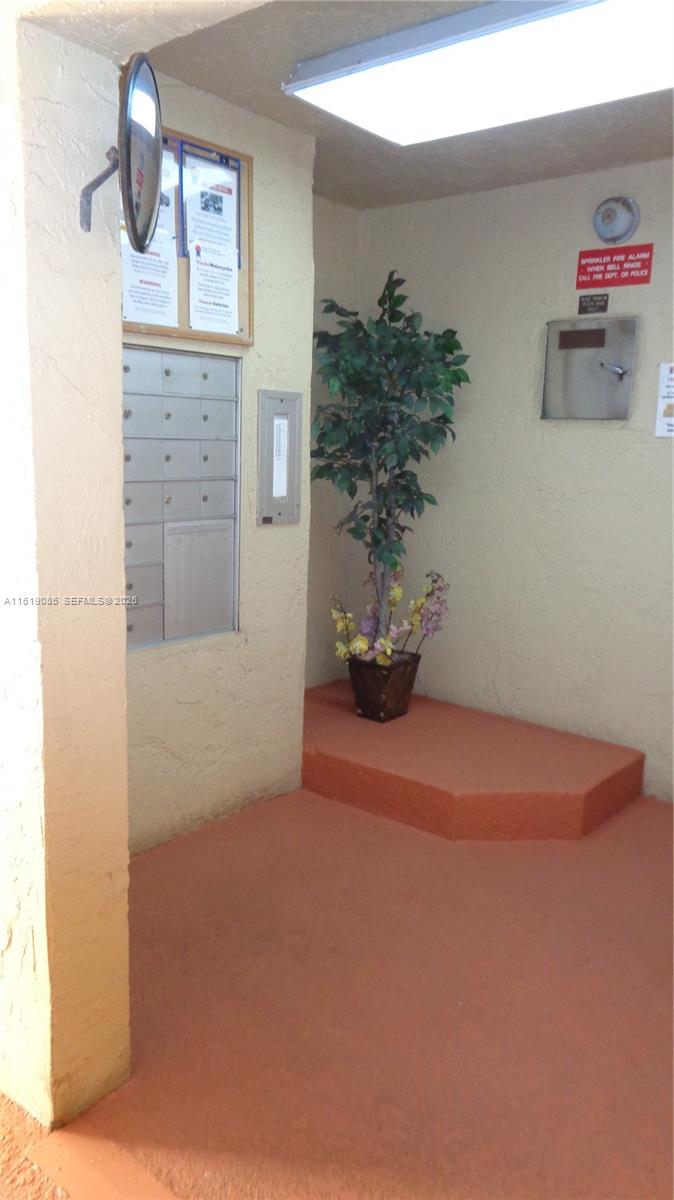 An indoor mailroom features a wall of metal mailboxes, a potted plant, and orange flooring — 6085 N Sabal Palm Blvd # 204, Tamarac FL 33319, TAMARAC, FL