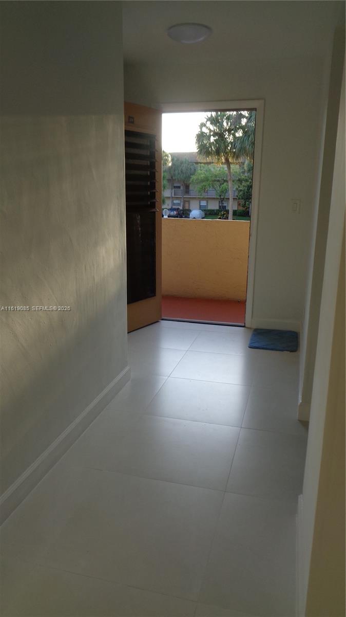 A tiled hallway leads to an open door revealing a balcony and outdoor residential buildings — 6085 N Sabal Palm Blvd # 204, Tamarac FL 33319, TAMARAC, FL