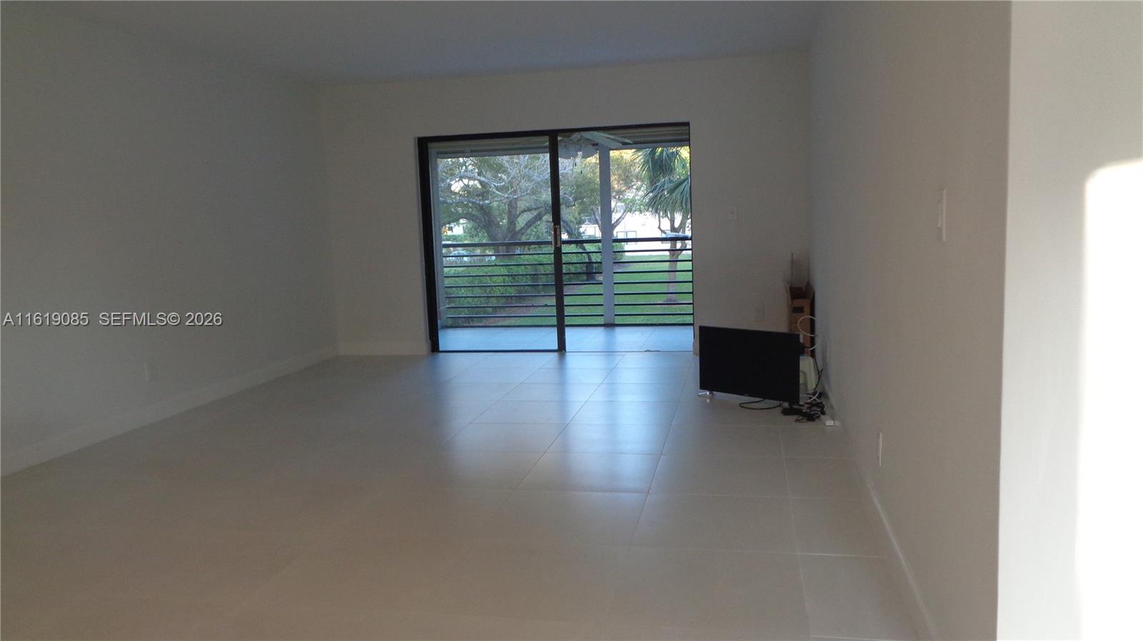 An empty room with light tile flooring features a sliding glass door leading to a balcony — 6085 N Sabal Palm Blvd # 204, Tamarac FL 33319, TAMARAC, FL