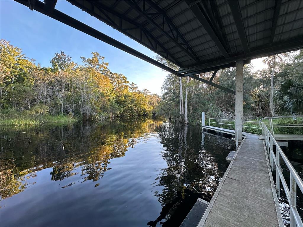 A wooden dock extends over dark water toward a wooded shoreline under a metal roof — 2924 BOATING BOULEVARD, KISSIMMEE, FL