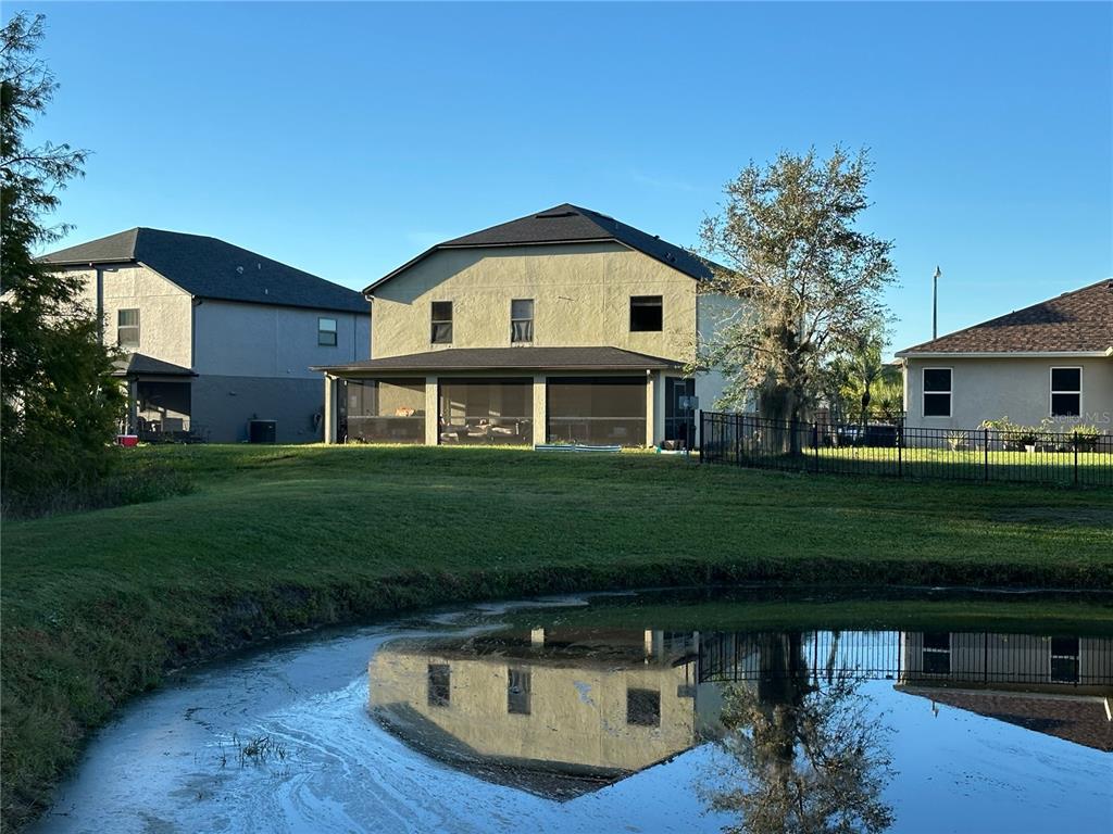 A two-story house with a screened-in porch sits behind a pond on a sunny day — 2924 BOATING BOULEVARD, KISSIMMEE, FL