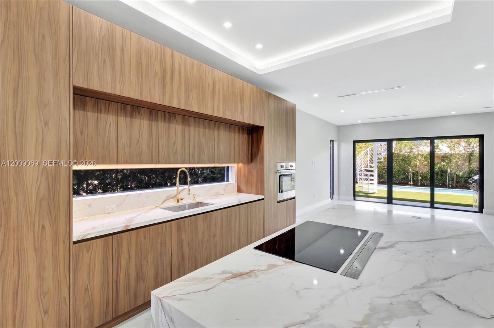 A modern kitchen features wood cabinetry, marble countertops, a central island, and floor-to-ceiling glass doors — 1223 SW 12th Ct # 1223, Miami FL 33135, MIAMI, FL