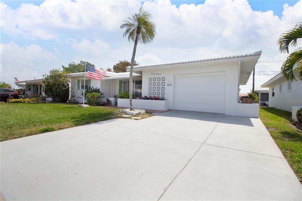A white single-story house features a concrete driveway, a palm tree, and an American flag — 4434 100TH AVENUE N, PINELLAS PARK, FL