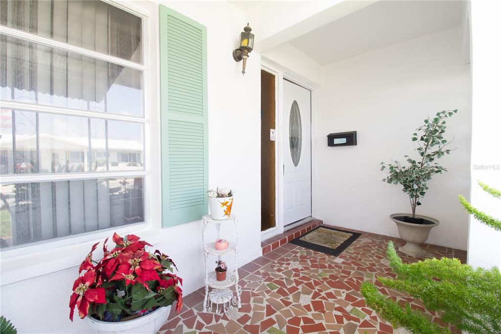 A covered front porch features a mosaic tile floor, a white door, and potted plants — 4434 100TH AVENUE N, PINELLAS PARK, FL