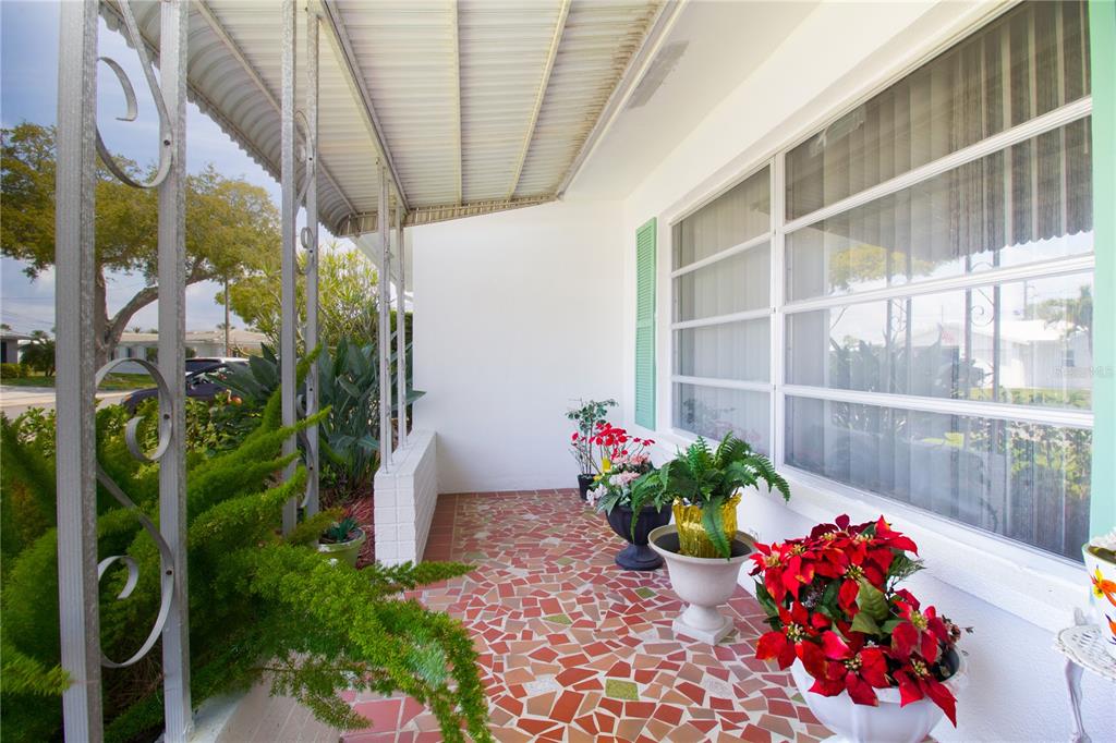 A covered porch features a red and white mosaic tile floor and decorative metal columns — 4434 100TH AVENUE N, PINELLAS PARK, FL
