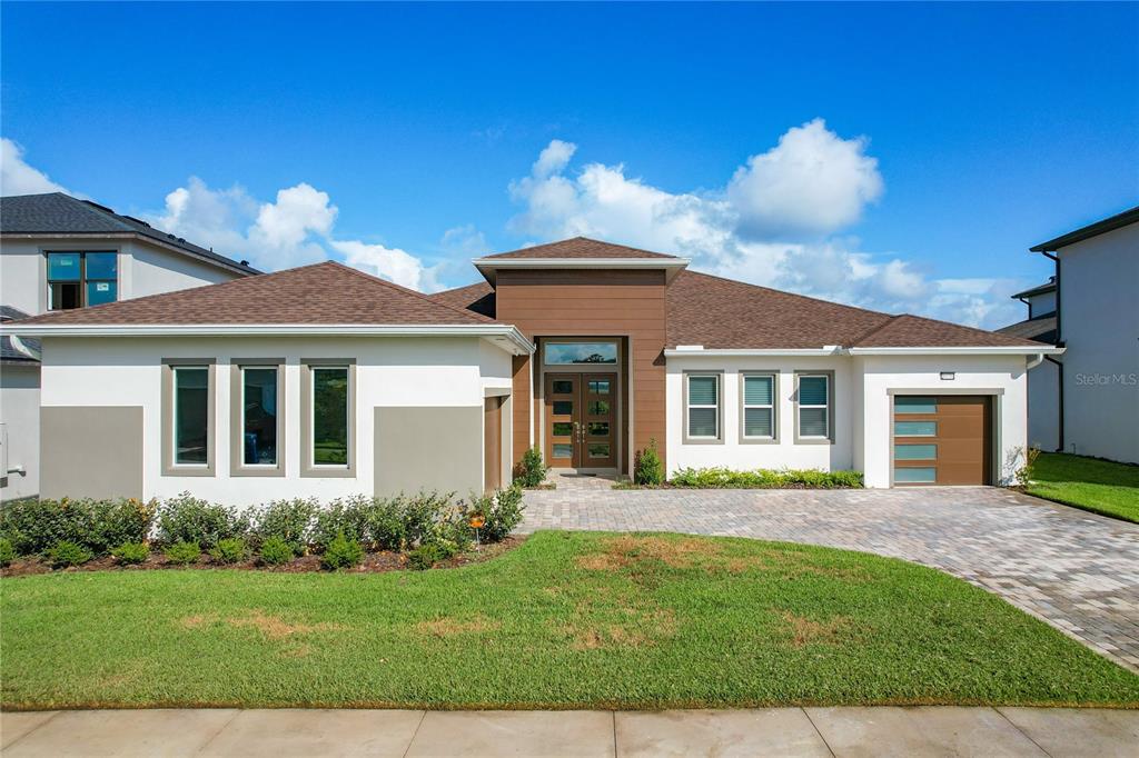A modern single-story house with a brown wood-paneled entryway, white stucco walls, and a driveway — 8859 IVY STARK BOULEVARD, WESLEY CHAPEL, FL