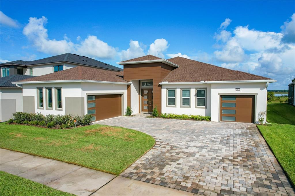 A modern single-story house with a paver driveway, two garages, and brown wood-look accents — 8859 IVY STARK BOULEVARD, WESLEY CHAPEL, FL