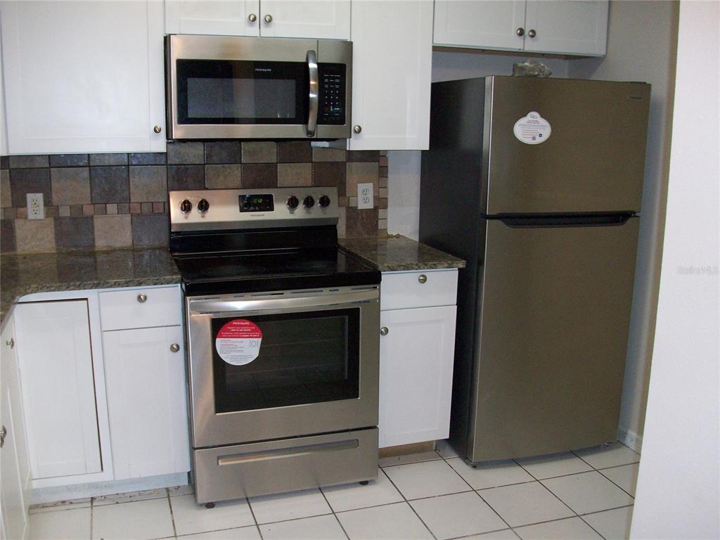 A kitchen features white cabinets, stainless steel appliances, granite countertops, and a tiled backsplash — 495 LAS CORTES LANE UNIT 105, ORLANDO, FL