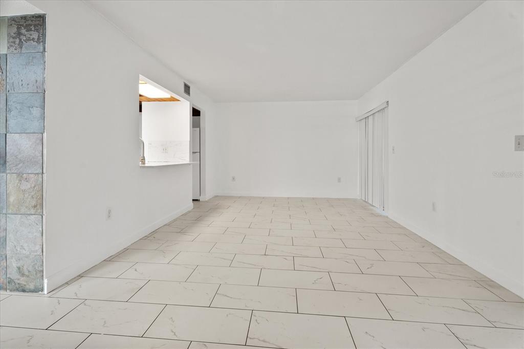An empty room with white walls, light-colored tile flooring, and a kitchen pass-through window — 140 ORCHID WOODS COURT UNIT 7A, DELTONA, FL