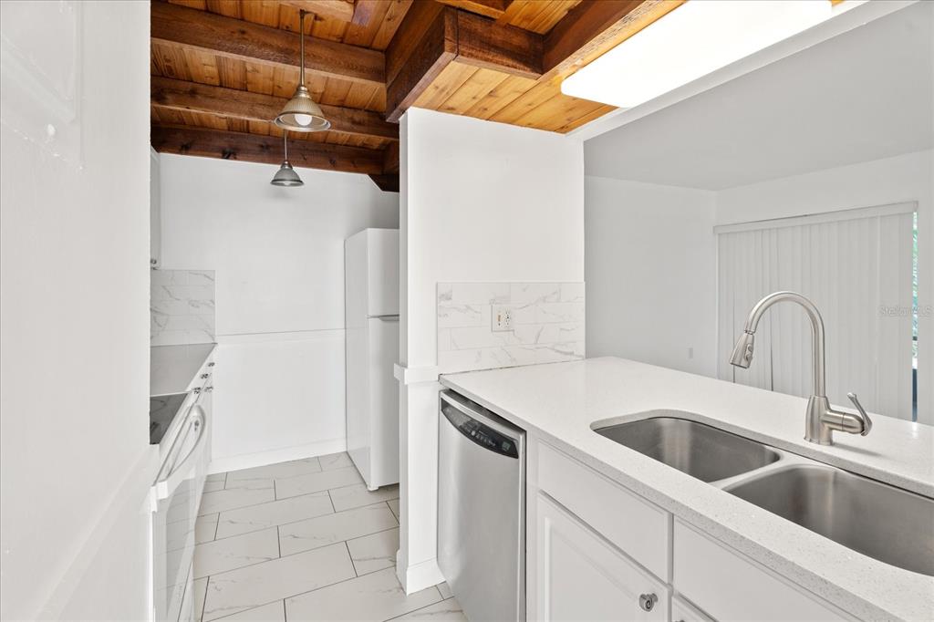 A kitchen features white cabinets, a stainless steel dishwasher, and a wood-paneled ceiling — 140 ORCHID WOODS COURT UNIT 7A, DELTONA, FL