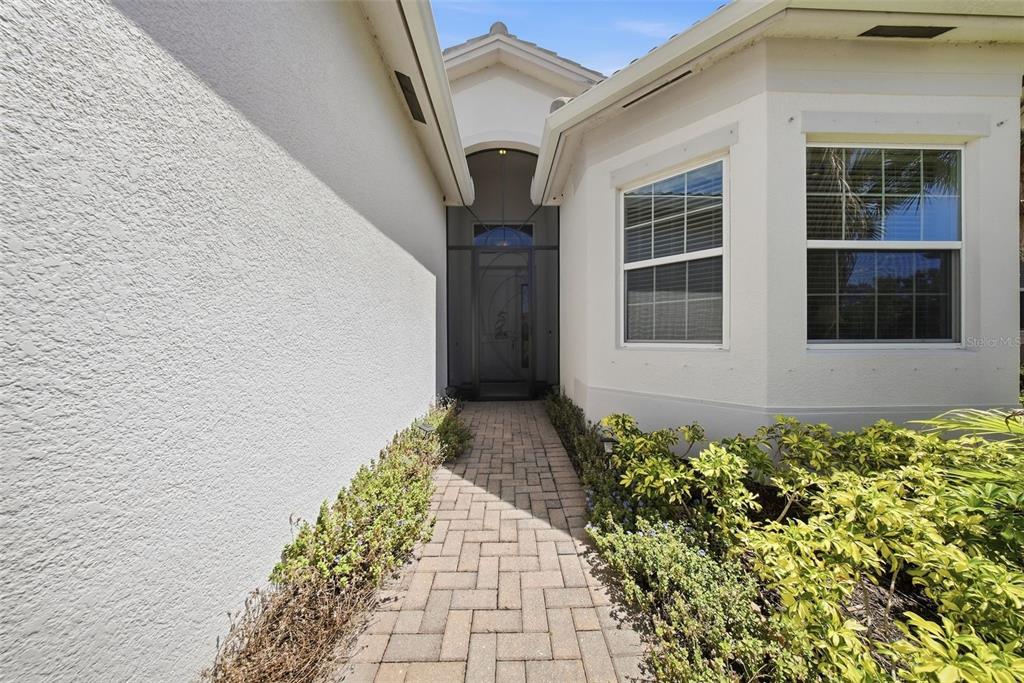 A paved walkway leads to the front entrance of a house with white stucco walls — 15528 CORONA DEL MAR DRIVE, WIMAUMA, FL