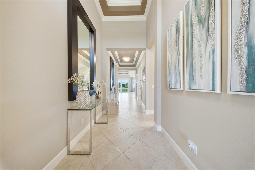 A long, tiled hallway features a glass console table, a large mirror, and wall art — 15528 CORONA DEL MAR DRIVE, WIMAUMA, FL