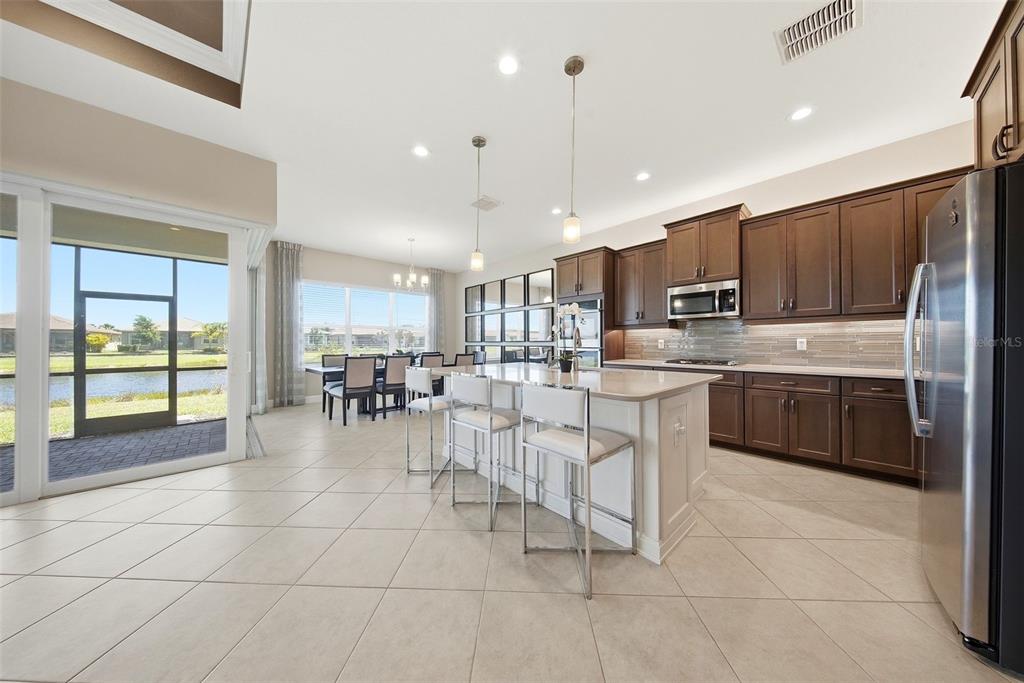 A kitchen with dark wood cabinets, a white island, and a dining area overlooking water — 15528 CORONA DEL MAR DRIVE, WIMAUMA, FL