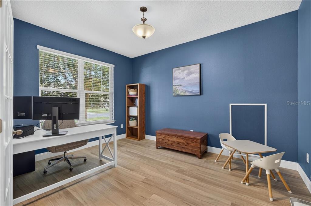 A home office with blue walls, wood-look flooring, a white desk, and a small table — 12209 W STREAMBED DRIVE, RIVERVIEW, FL