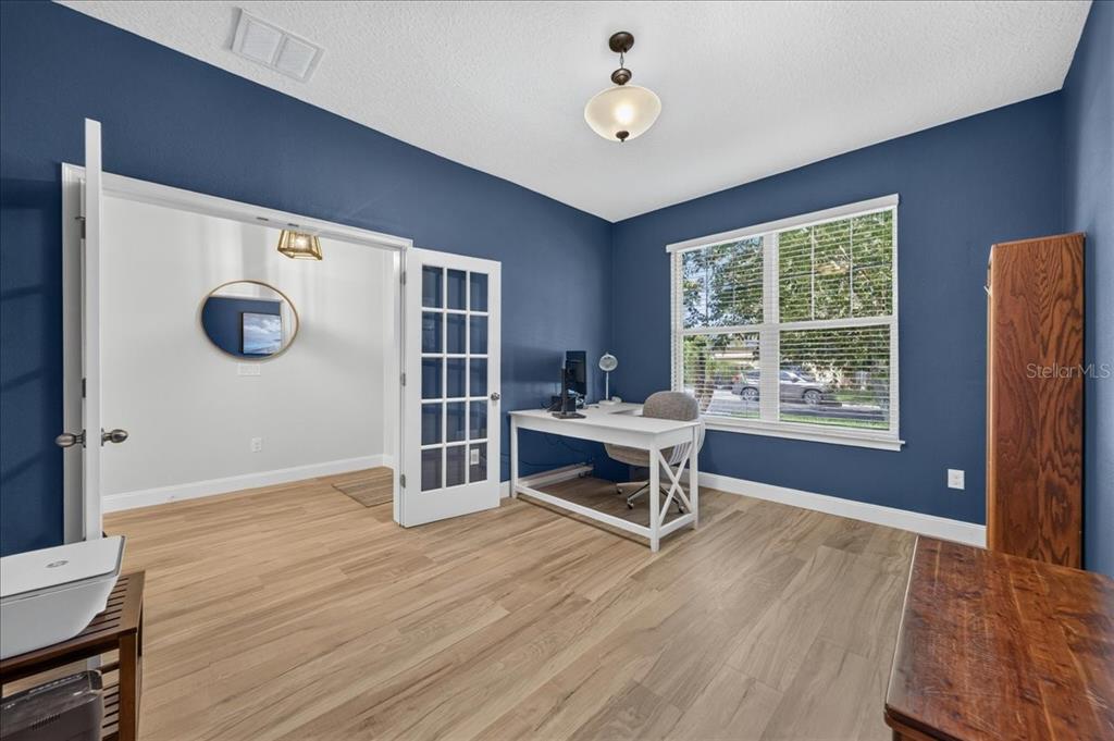 A home office features blue walls, light wood flooring, a white desk, and French doors — 12209 W STREAMBED DRIVE, RIVERVIEW, FL