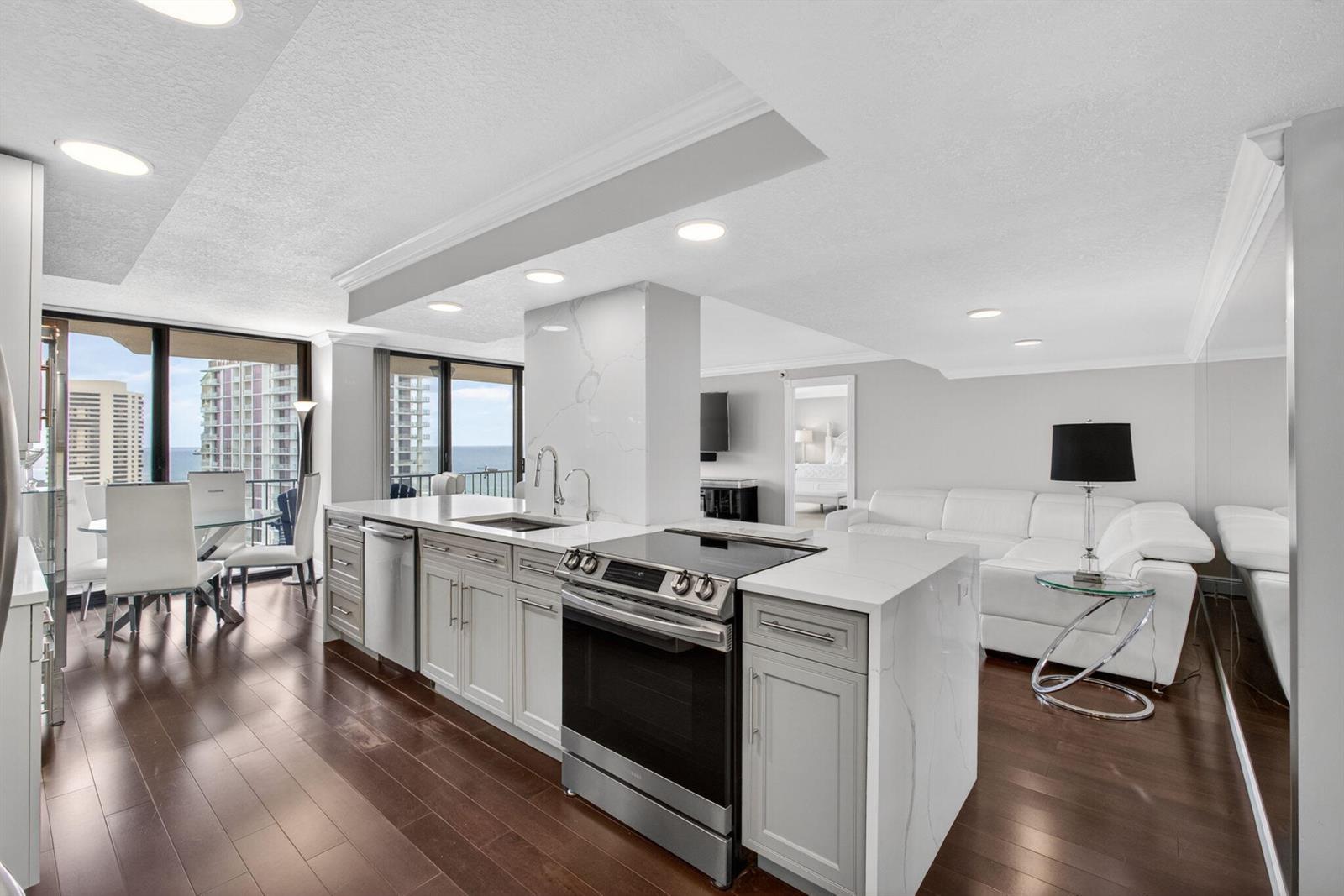 A modern kitchen with white marble countertops and stainless steel appliances overlooks a living area — 4200 N Ocean # 1706, Singer Island FL 33404, SINGER ISLAND, FL