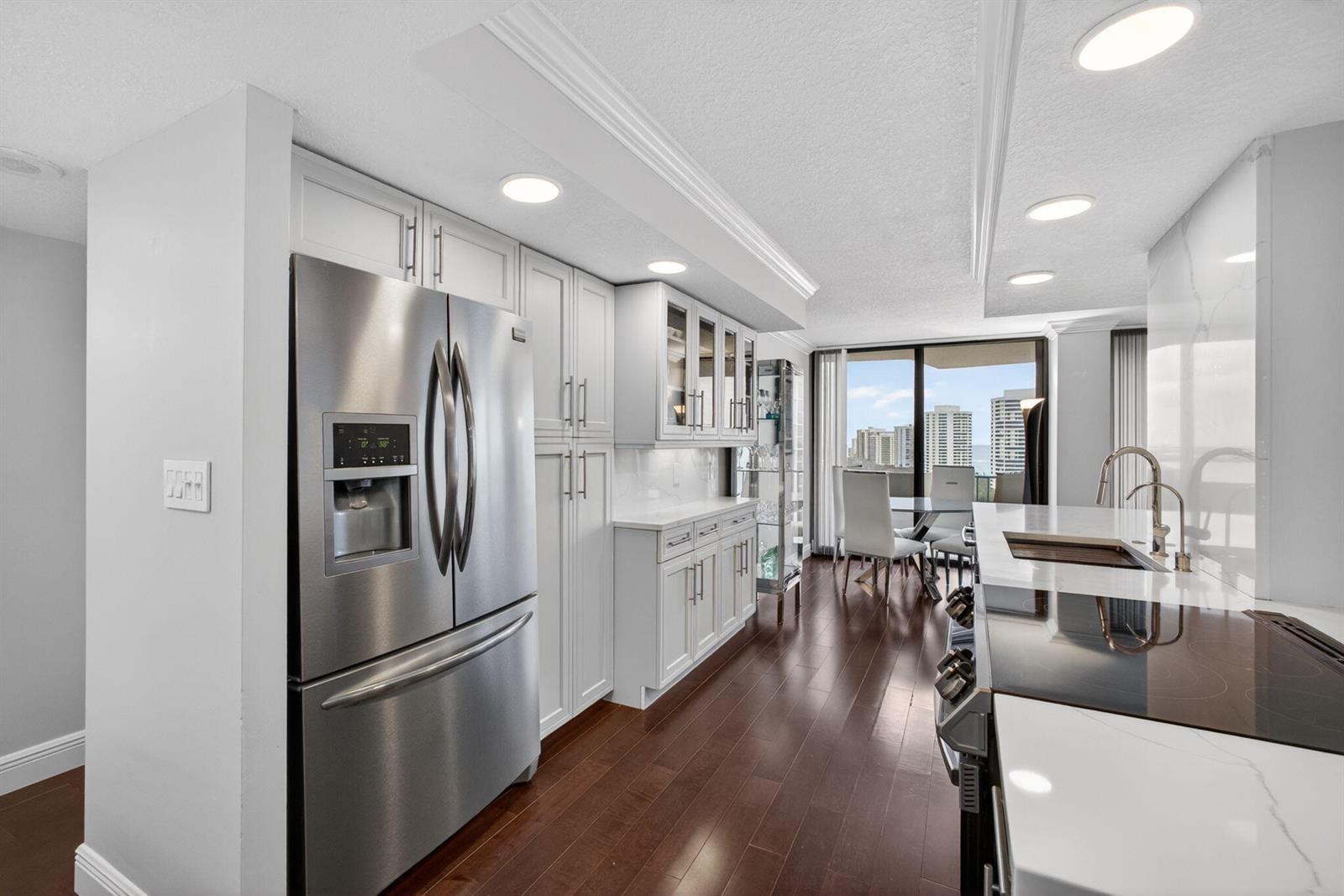 A modern kitchen features white cabinetry, stainless steel appliances, and dark wood flooring — 4200 N Ocean # 1706, Singer Island FL 33404, SINGER ISLAND, FL