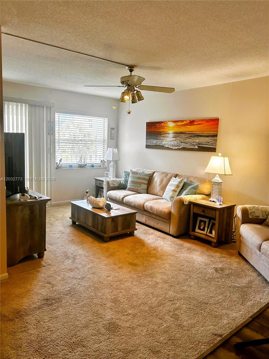 A living room features a beige sofa, a coffee table, and a sunset wall painting — 1750 Jefferson St # 303, Hollywood FL 33020, HOLLYWOOD, FL