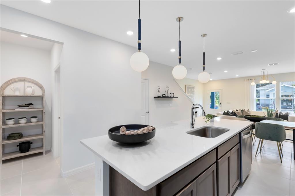 A kitchen island with a sink and pendant lights sits in an open-concept living space — 11478 NONA SOUND ST, ORLANDO, FL