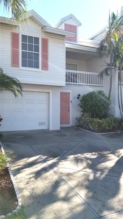 A two-story townhouse exterior features white siding, a single-car garage, and pink shutters and door — 153 SUN ISLE CIRCLE, TREASURE ISLAND, FL