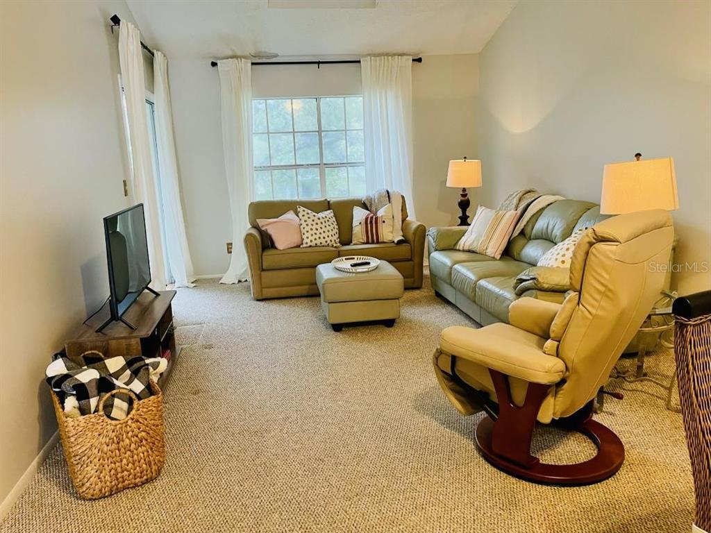 A living room features carpeted flooring, a sofa, a recliner, and a television on a stand — 153 SUN ISLE CIRCLE, TREASURE ISLAND, FL