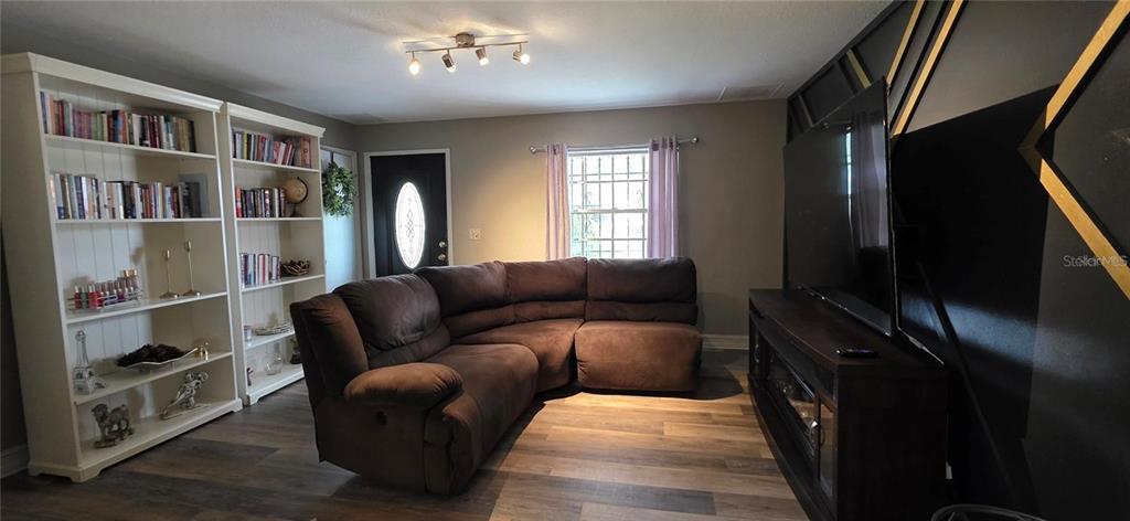 A living room features a brown sectional sofa, two white bookshelves, and a dark accent wall — 1302 CENTER STREET, OCOEE, FL
