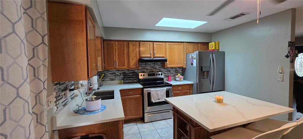 A kitchen features wood cabinets, stainless steel appliances, a white island, and a tiled backsplash — 1302 CENTER STREET, OCOEE, FL