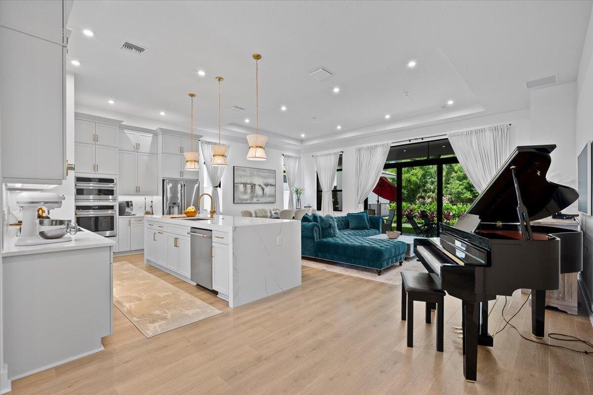 A modern open-concept kitchen and living area features a grand piano and teal sofa — 6870 SE Haven Lane, Stuart FL 34997, STUART, FL