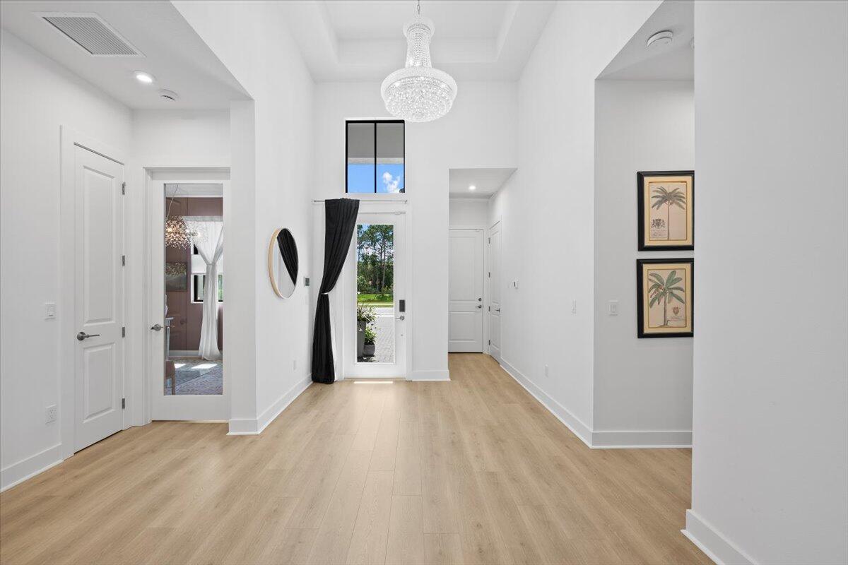 A bright, high-ceilinged entryway features light wood flooring, a crystal chandelier, and white walls — 6870 SE Haven Lane, Stuart FL 34997, STUART, FL