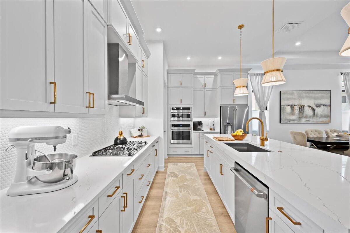 A modern white kitchen features gold hardware, quartz countertops, and a large central island — 6870 SE Haven Lane, Stuart FL 34997, STUART, FL