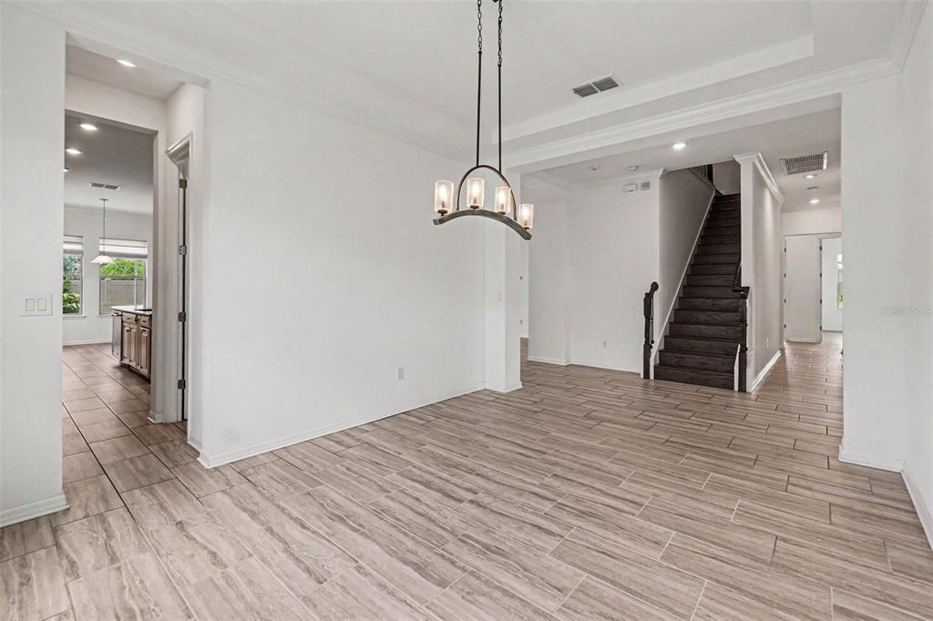 A dining area features light wood-look tile flooring, a modern chandelier, and a dark staircase — 13065 BLISS LOOP, BRADENTON, FL