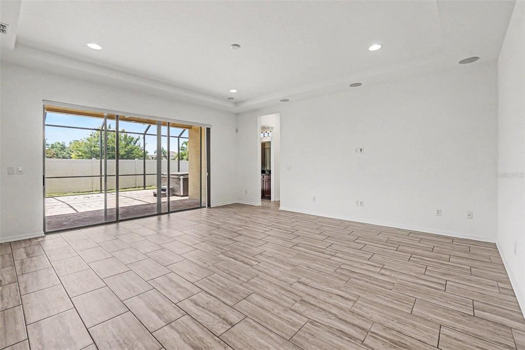A bright, empty living room features wood-look tile flooring, recessed lighting, and sliding glass doors — 13065 BLISS LOOP, BRADENTON, FL