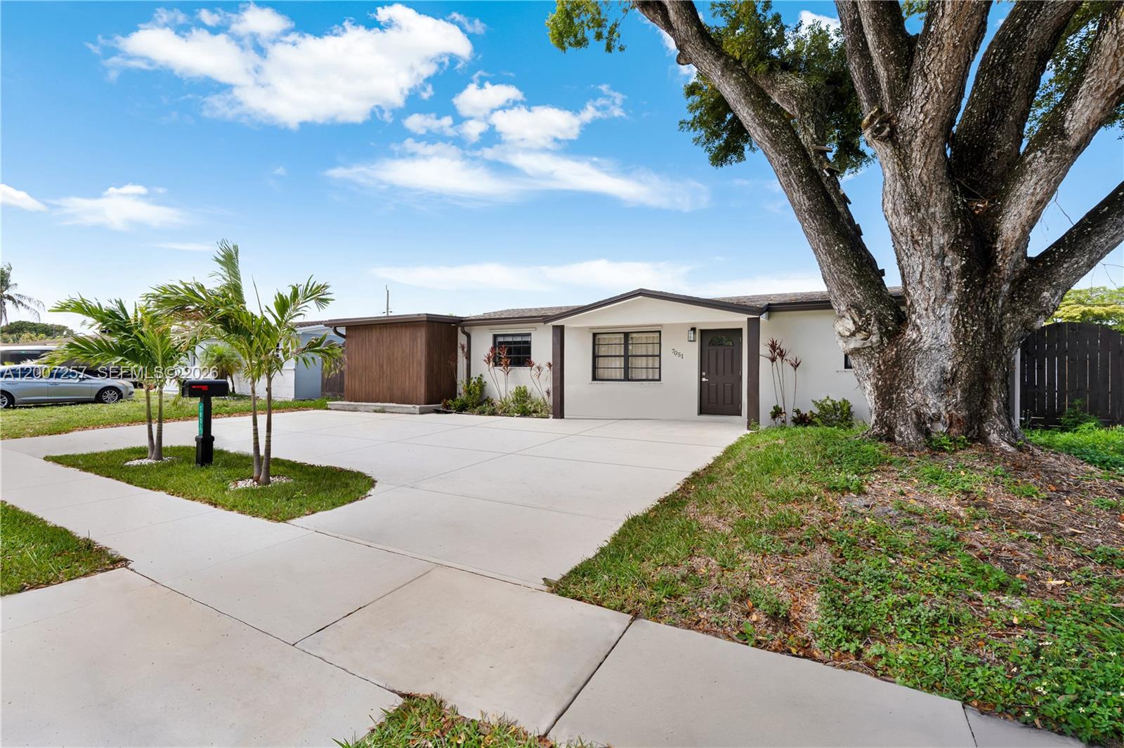A single-story house with a concrete driveway, a large tree, and palm trees in front — 7051 Tyler St, Hollywood FL 33024, HOLLYWOOD, FL