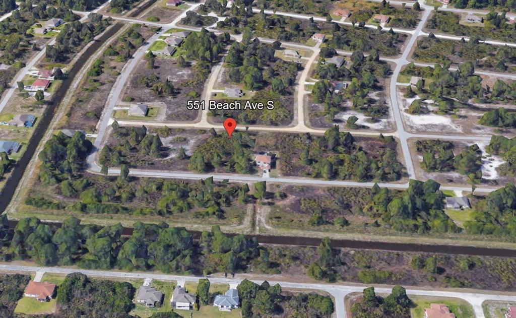 An aerial view shows a residential lot with scattered trees and a single house — 551 BEACH AVENUE S, LEHIGH ACRES, FL