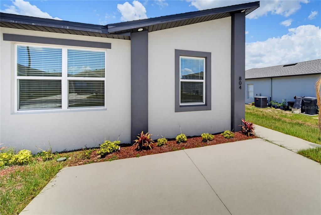 A modern house exterior features white stucco walls, dark gray trim, and a concrete driveway — 804 COLVILLE DRIVE, KISSIMMEE, FL