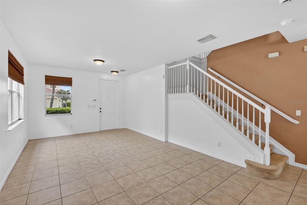 An empty living room features tile flooring, white walls, and a staircase with carpeted steps — 4197 RIVER BANK WAY, PUNTA GORDA, FL