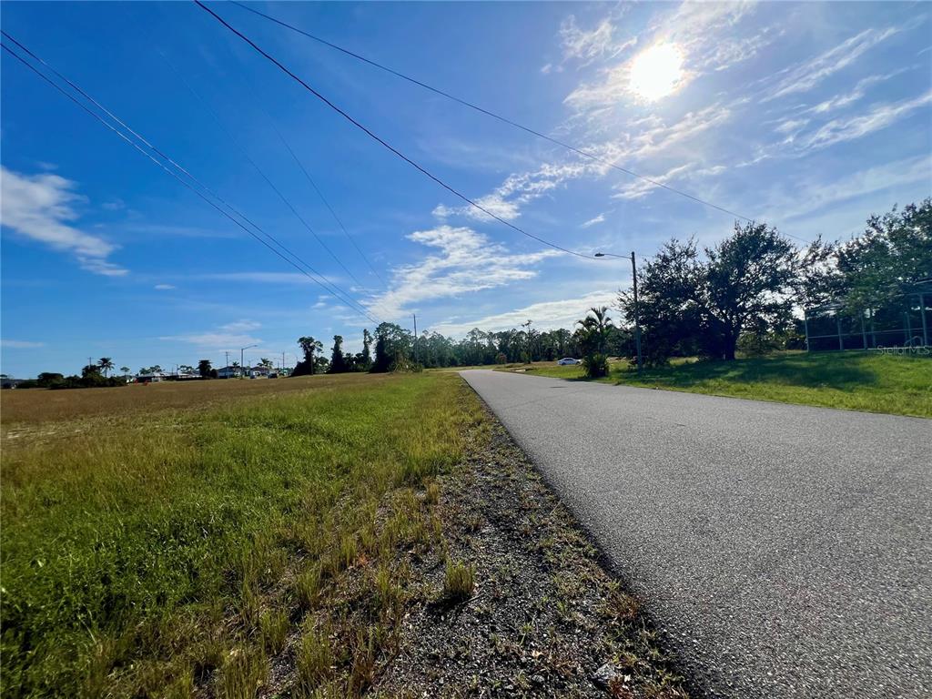A paved road runs alongside a grassy, undeveloped lot under a bright, sunny sky — 1515 NE 32ND LANE, CAPE CORAL, FL