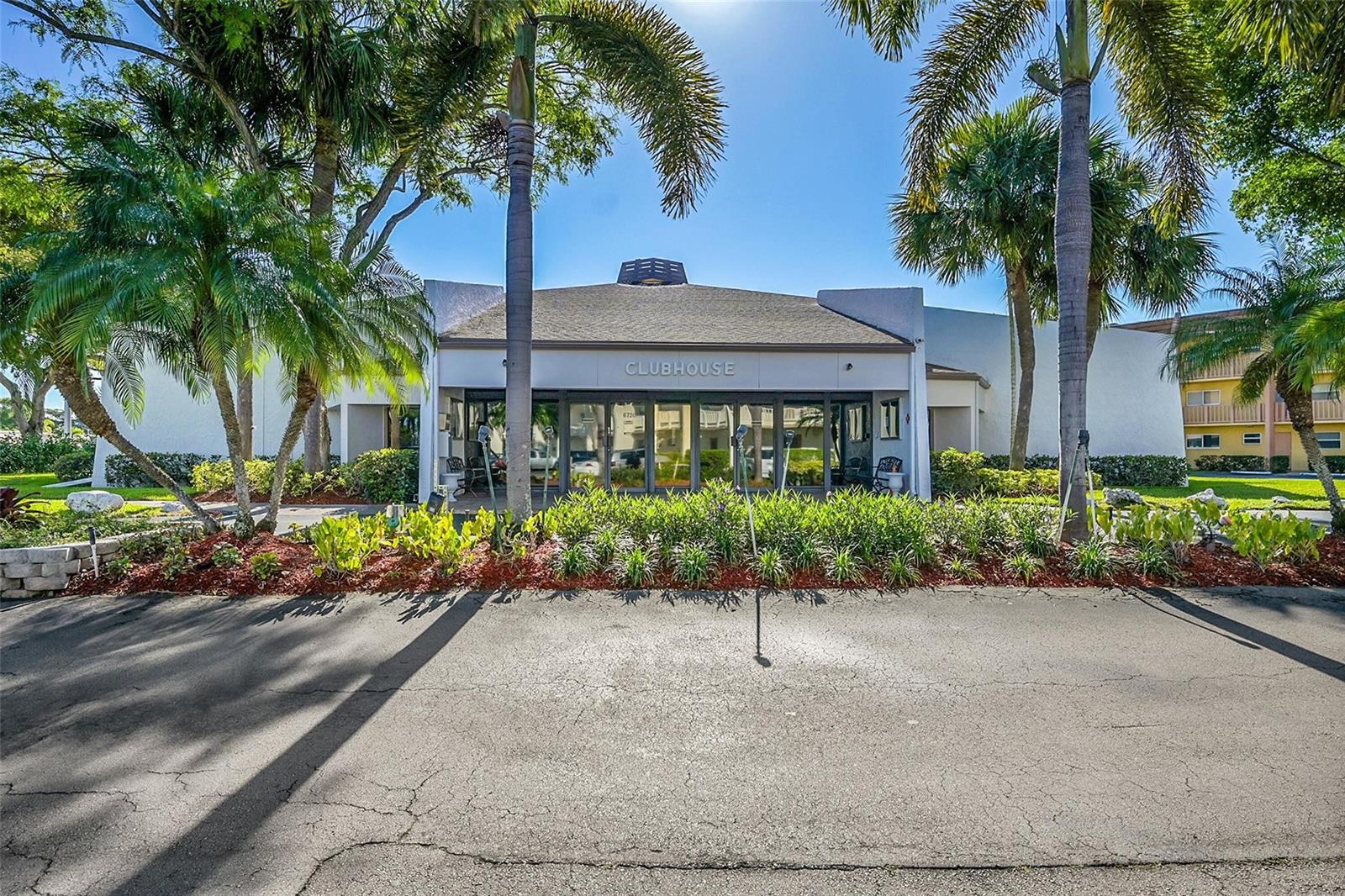 A single-story clubhouse building features a glass-paneled entrance surrounded by palm trees and landscaping — 6800 Royal Palm Boulevard # 102, Margate FL 33063, MARGATE, FL