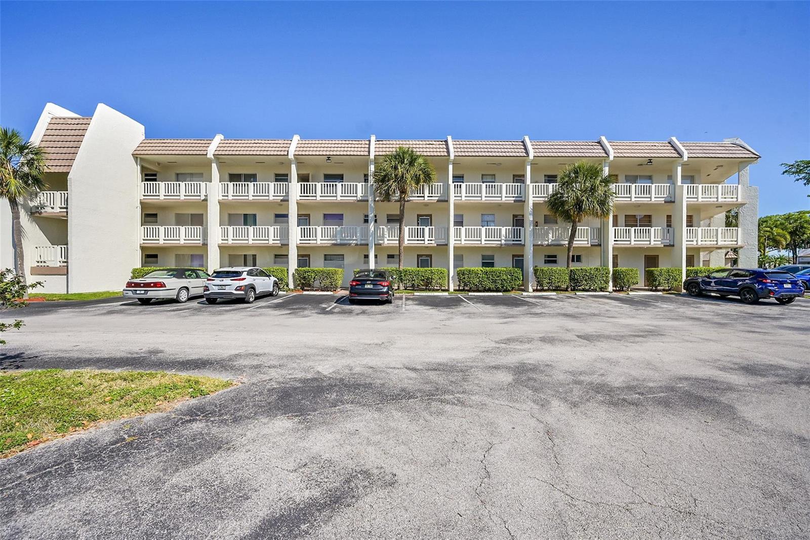 A three-story apartment building with white balconies and a parking lot in the foreground — 6800 Royal Palm Boulevard # 102, Margate FL 33063, MARGATE, FL