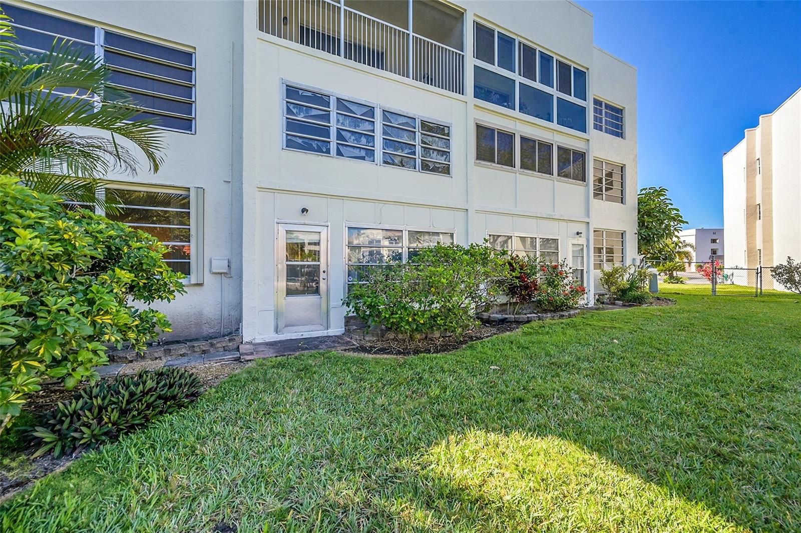 The exterior of a multi-story apartment building features a ground-level patio door and green lawn — 6800 Royal Palm Boulevard # 102, Margate FL 33063, MARGATE, FL