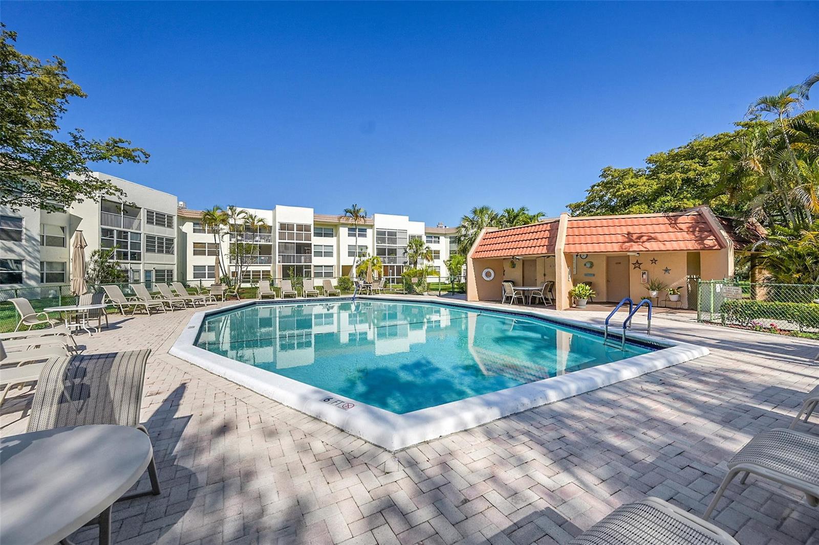 A rectangular swimming pool sits on a paved patio surrounded by apartment buildings and landscaping — 6800 Royal Palm Boulevard # 102, Margate FL 33063, MARGATE, FL