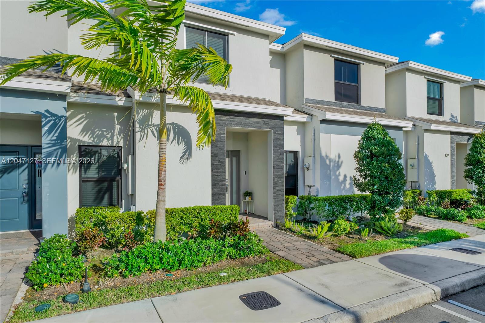 A row of modern two-story townhouses features light-colored stucco facades, stone accents, and manicured landscaping — 117 NE 3rd Ct, Florida City FL 33034, FLORIDA CITY, FL