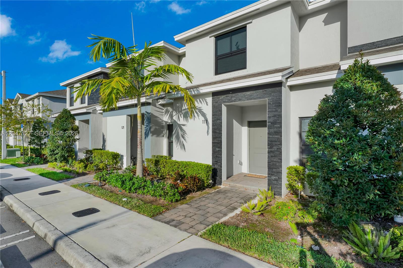 A two-story townhouse exterior features a gray front door, stone accents, and a palm tree — 117 NE 3rd Ct, Florida City FL 33034, FLORIDA CITY, FL