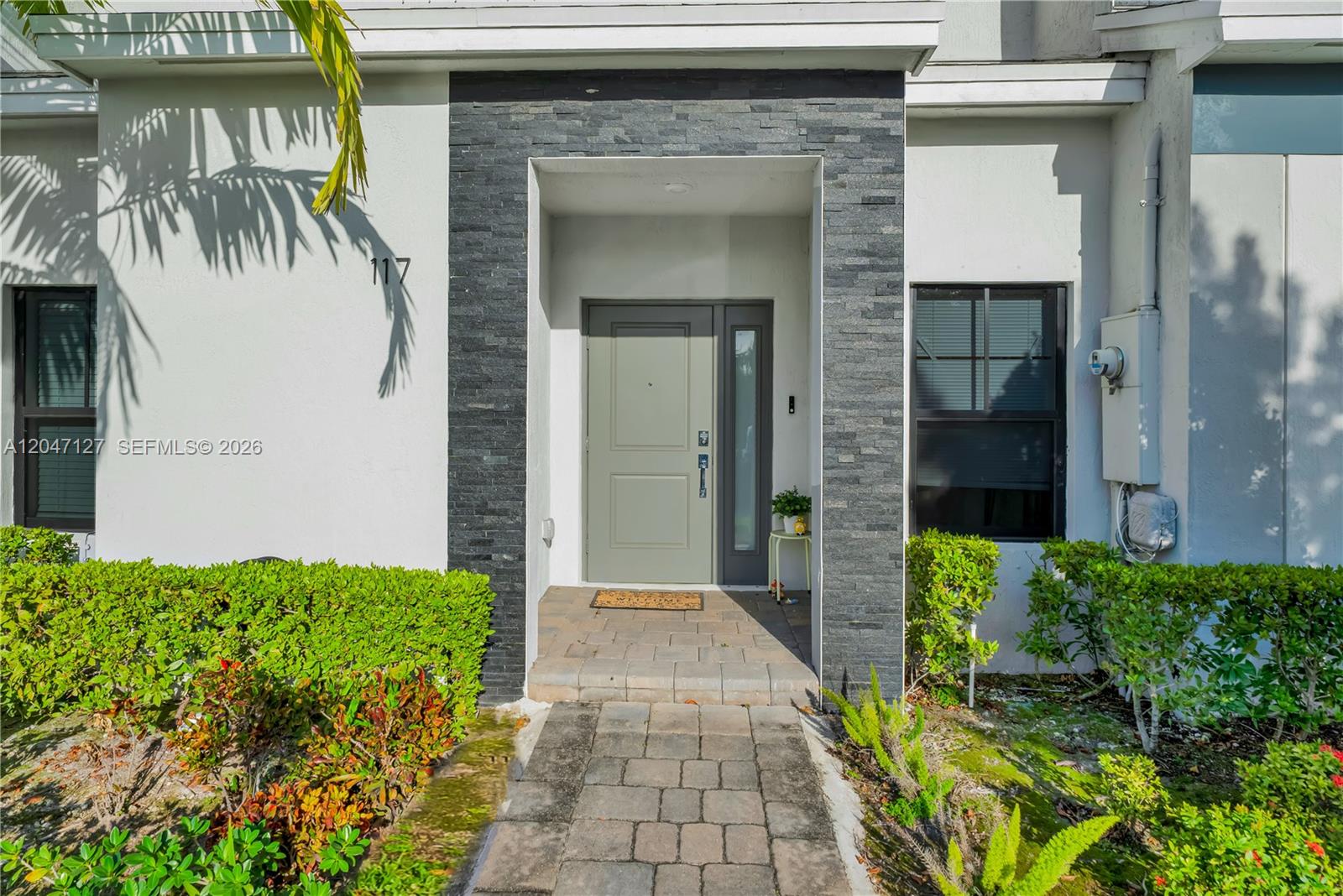 The exterior of a home features a stone-accented entryway, a gray door, and landscaping — 117 NE 3rd Ct, Florida City FL 33034, FLORIDA CITY, FL