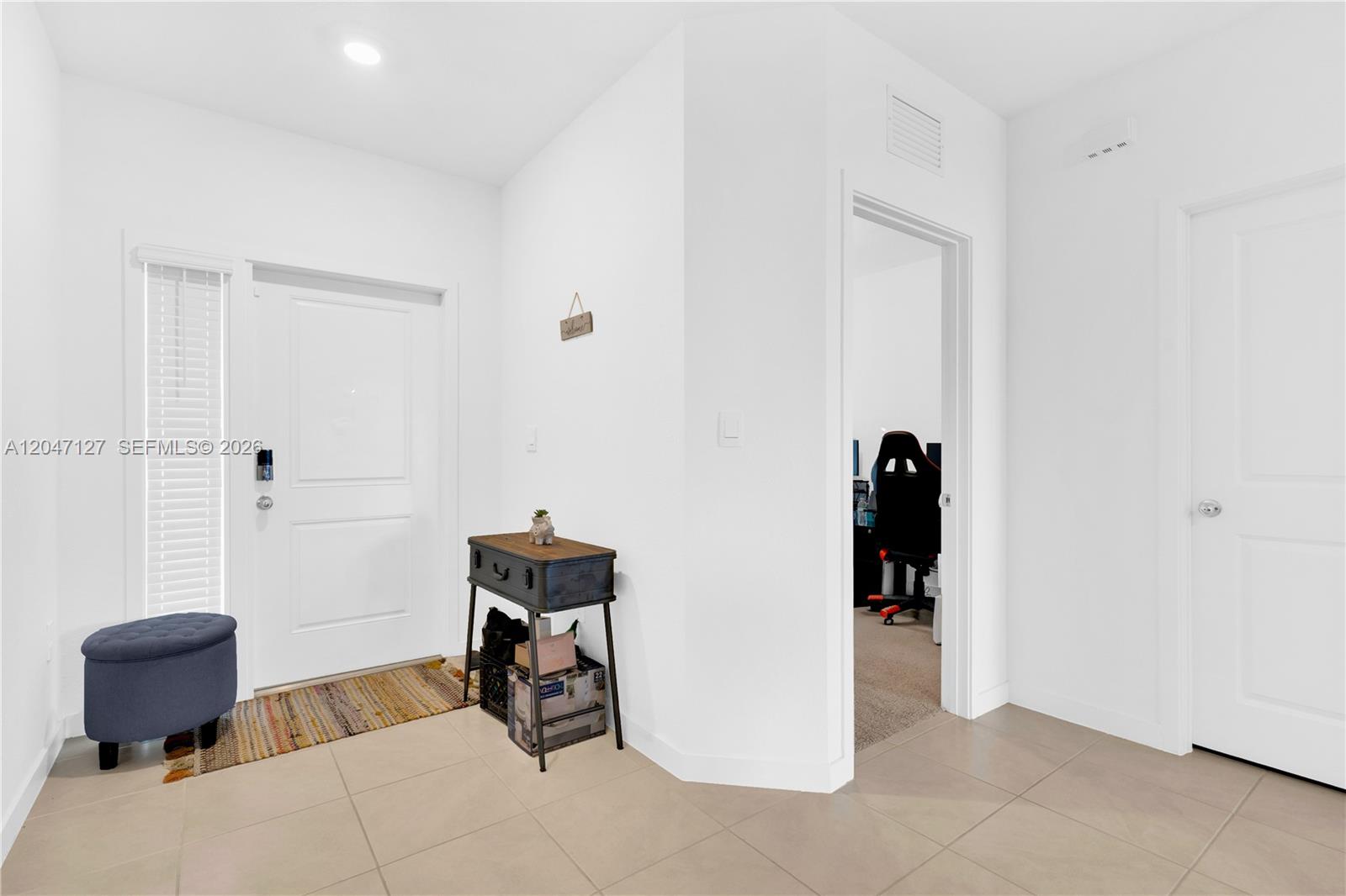 A bright entryway features a white door, tiled floors, a small console table, and a doorway — 117 NE 3rd Ct, Florida City FL 33034, FLORIDA CITY, FL
