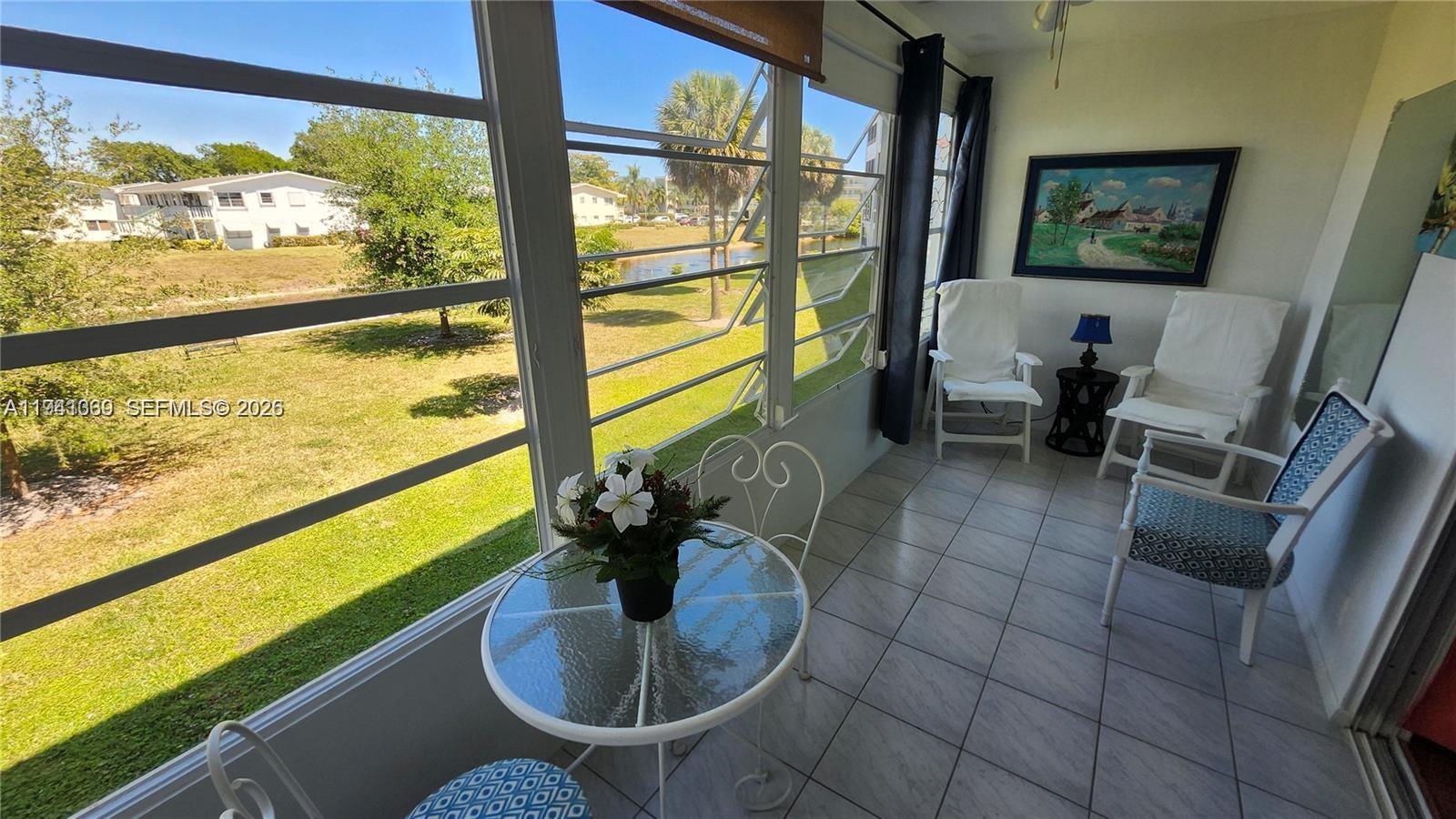 A sunroom features tile flooring, a small glass table, and large windows overlooking a lawn — 2112 Newport U # 2112, Deerfield Beach FL 33442, DEERFIELD BEACH, FL