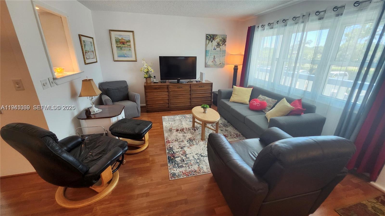 A living room features a gray sofa, leather armchairs, a television console, and hardwood floors — 2112 Newport U # 2112, Deerfield Beach FL 33442, DEERFIELD BEACH, FL